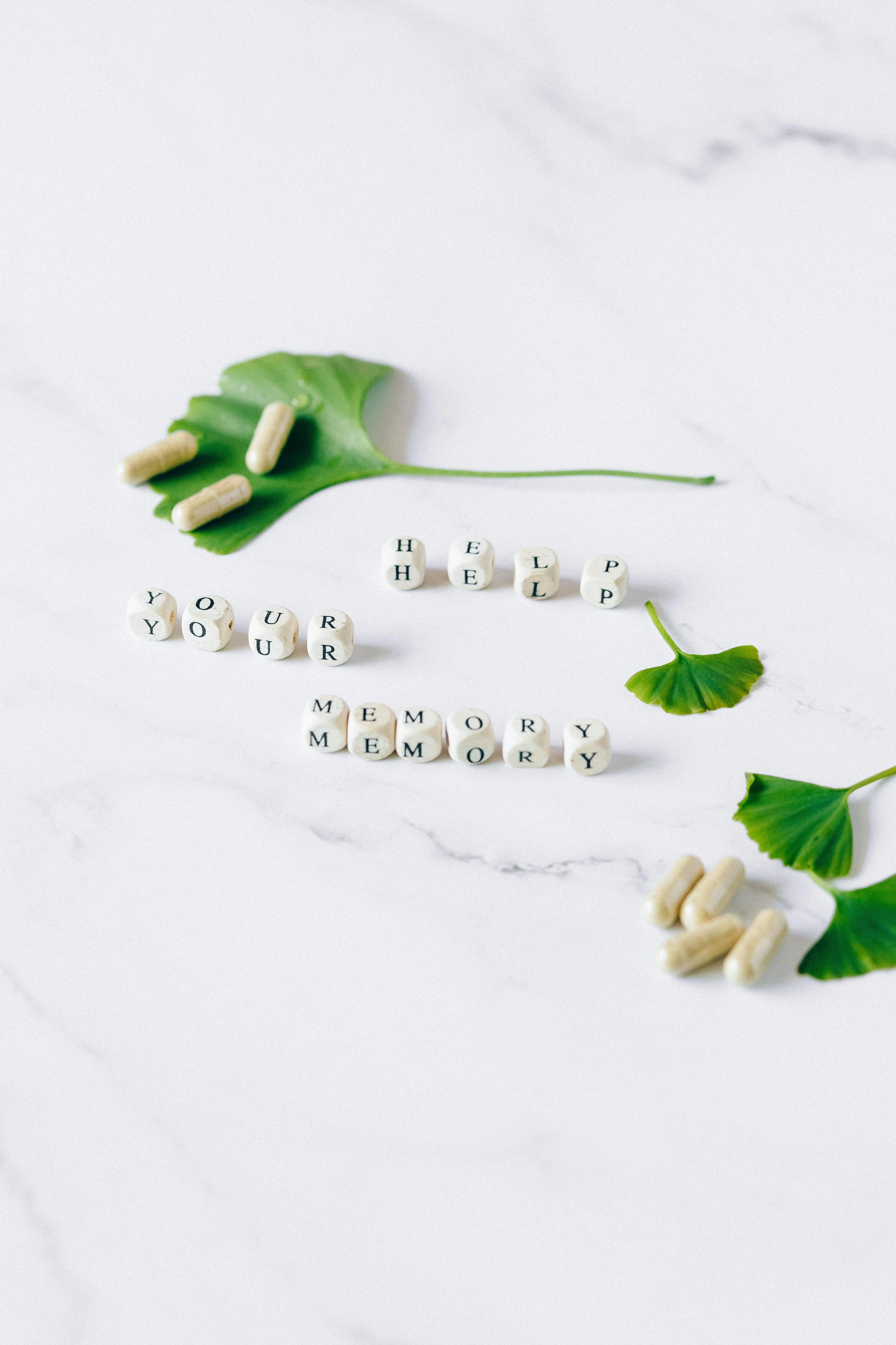 Ginkgo biloba leaves and herbal capsules arranged on a white surface