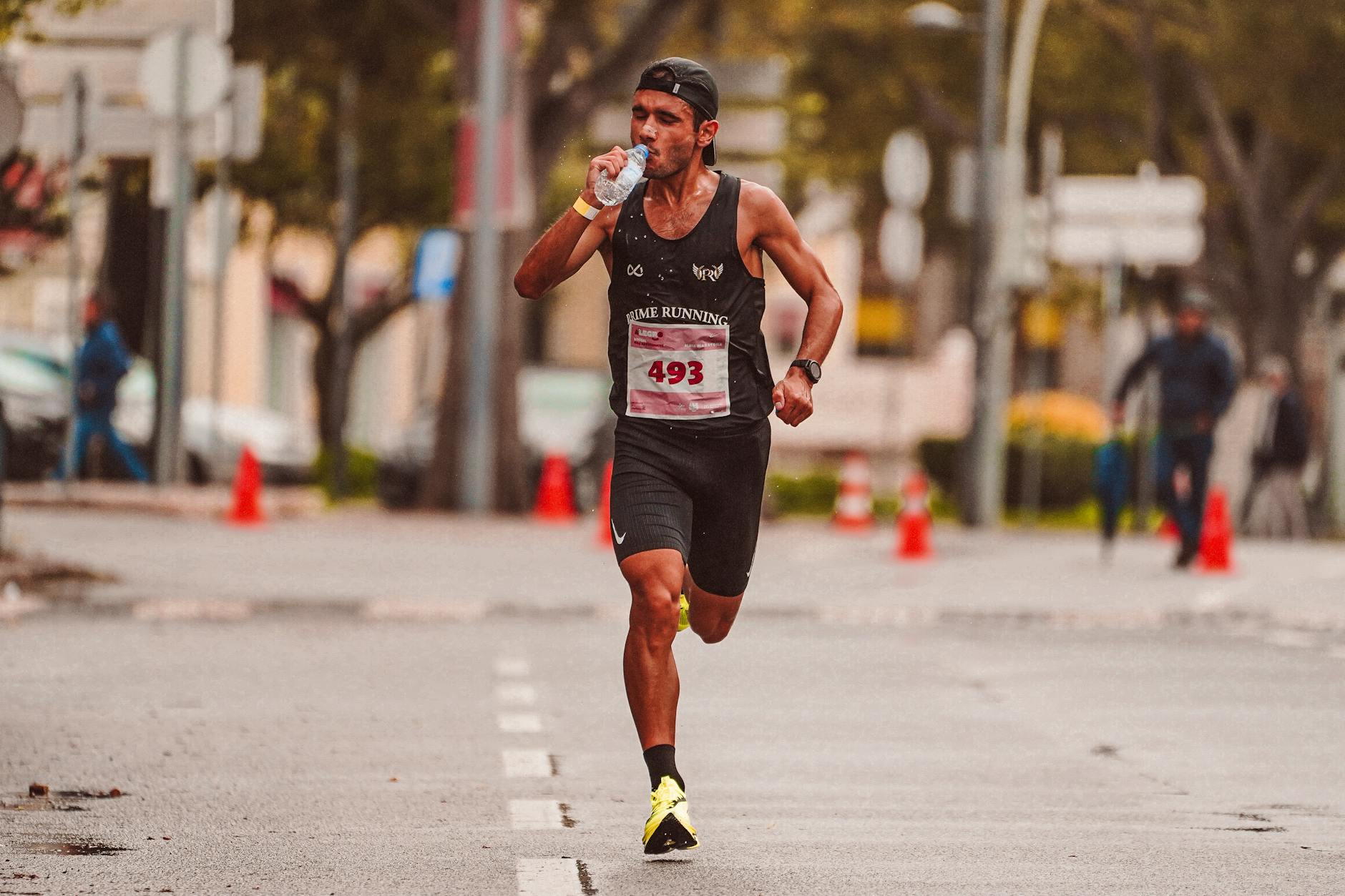Athlete running a marathon on a city street, hydrating from a water cup mid-race