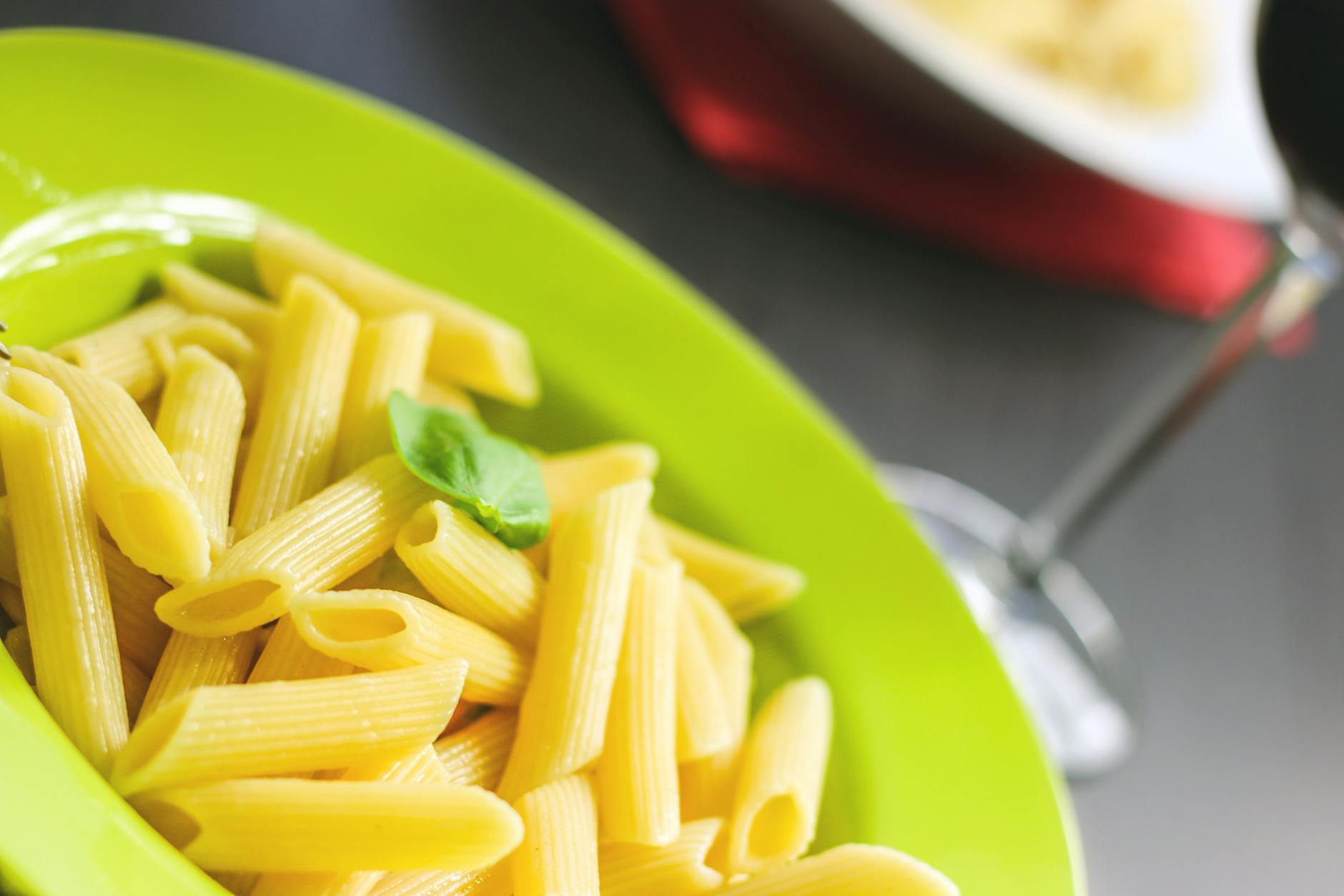Close-up of penne pasta with basil on a plate, representing carbohydrate-rich pre-race fuel for endurance runners