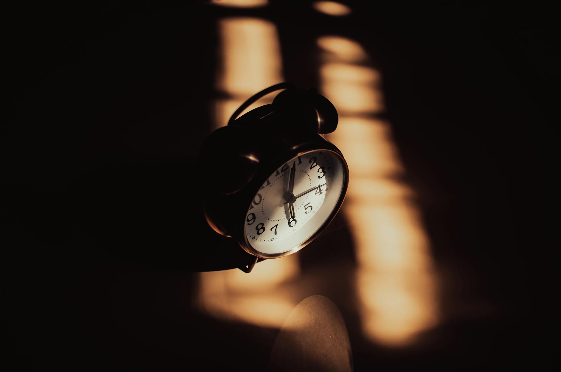 A retro analog alarm clock in moody shadows and warm lighting, evoking sleep and circadian rhythm